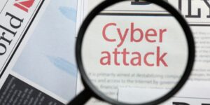 Justdata ICT, Een vergrootglas richt zich op de woorden Cyberaanval in grote rode letters op een krantenpagina, om de toenemende dreiging van slimme aanvallen en de noodzaak van sterke cyberbeveiliging te benadrukken.
