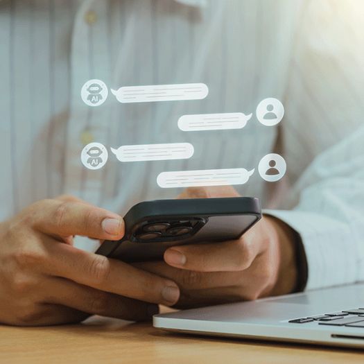 Justdata ICT, Een persoon houdt een smartphone vast in de buurt van een laptop, met digitale chatbellen die boven de telefoon zweven, symboliserend hoe kunstmatige intelligentie communicatie en digitale toekomst binnen handbereik brengt.